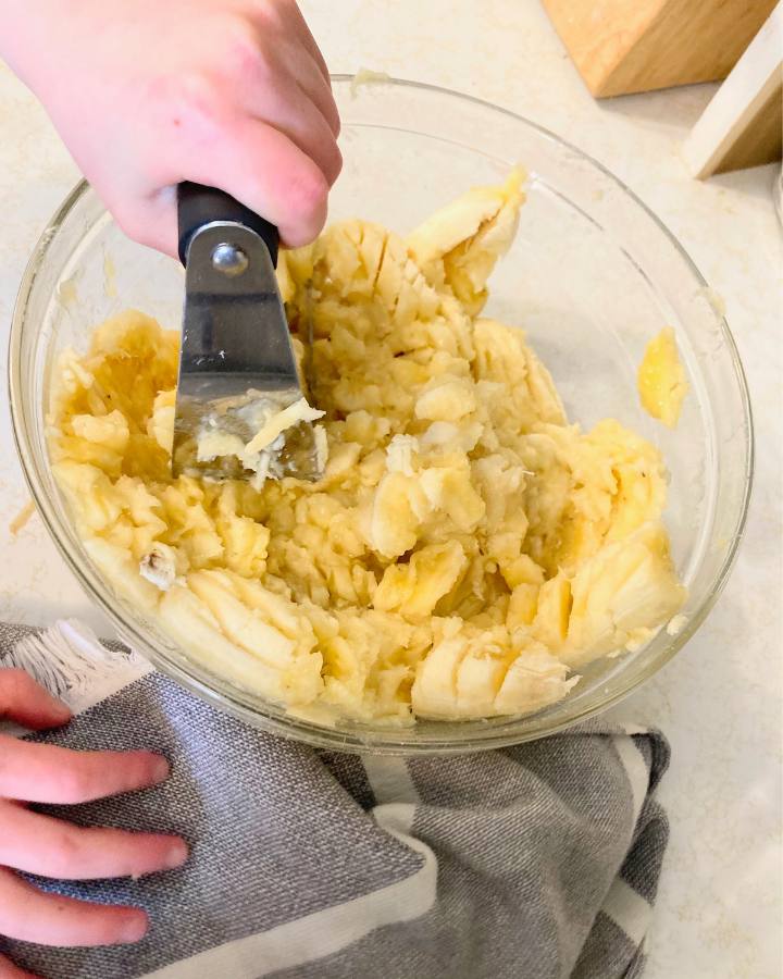 mashing the bowl of bananas with a pastry blender
