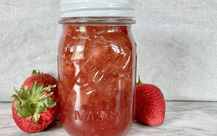 strawberry rhubarb freezer jam in a mason jar on a grey towel with fresh strawberries