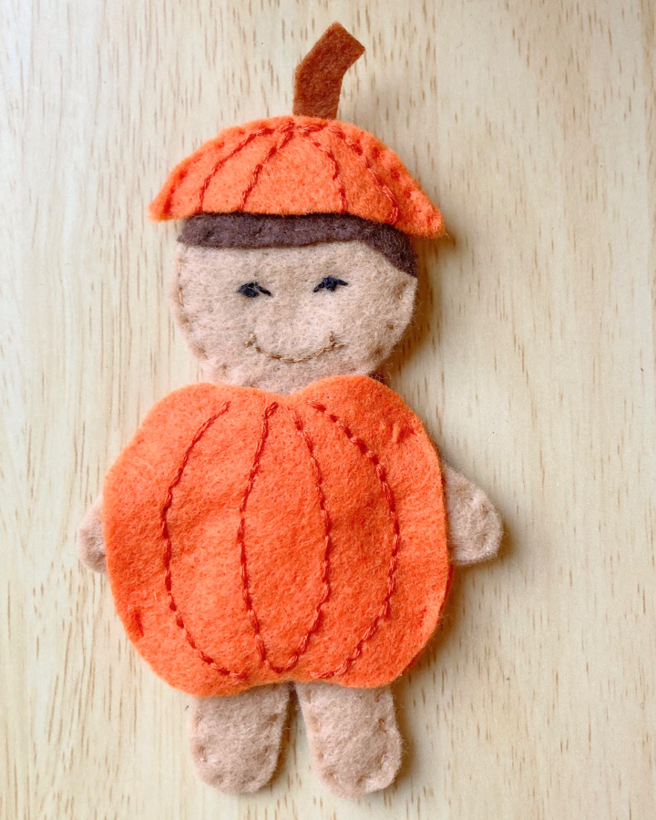 A felt doll wearing a felt pumpkin costume around his middle and a pumpkin stem hat