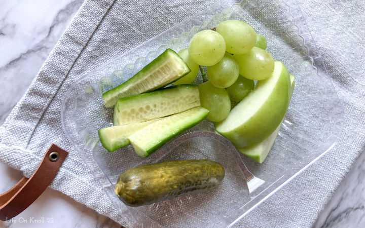 Green fruits and vegetables in a plastic tray on a grey towel