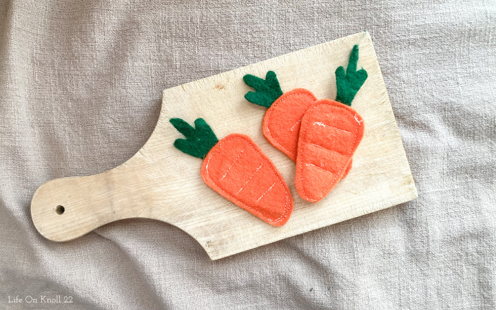 felt play carrots arranged on a wooden cutting board on a grey tablecloth