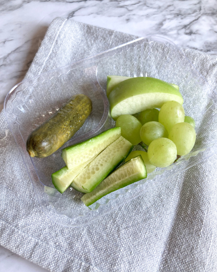 Green grapes, apple slices, cucumbers and a pickle in a plastic nacho tray.
